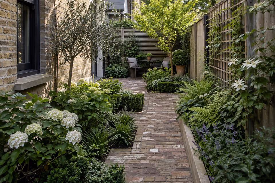 Narrow urban townhouse garden with alternating planting beds and brick paving, slim trellis on boundary and a small sitting nook at far end