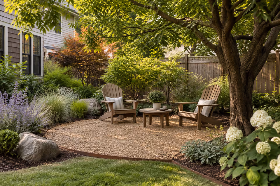 Contained golden gravel garden seating area with steel edging, two timber Adirondack chairs and low table under mature tree, no firepit